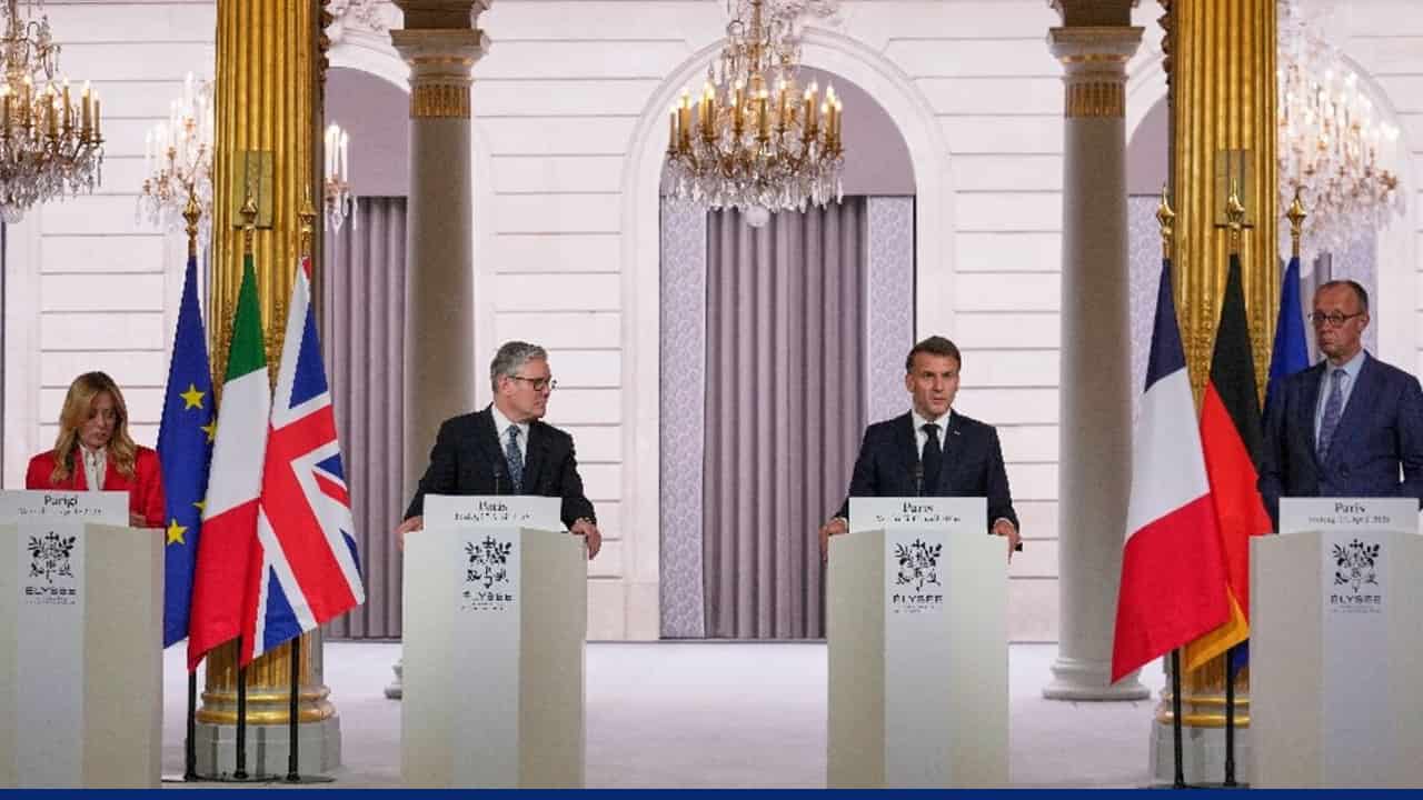 Leaders stand at podiums during a formal press conference at the ΓlysΓ©e Palace, with national flags of the European Union, Italy, United Kingdom, France, and Germany displayed behind them. Elegant chandeliers and gold-trimmed columns frame the setting.